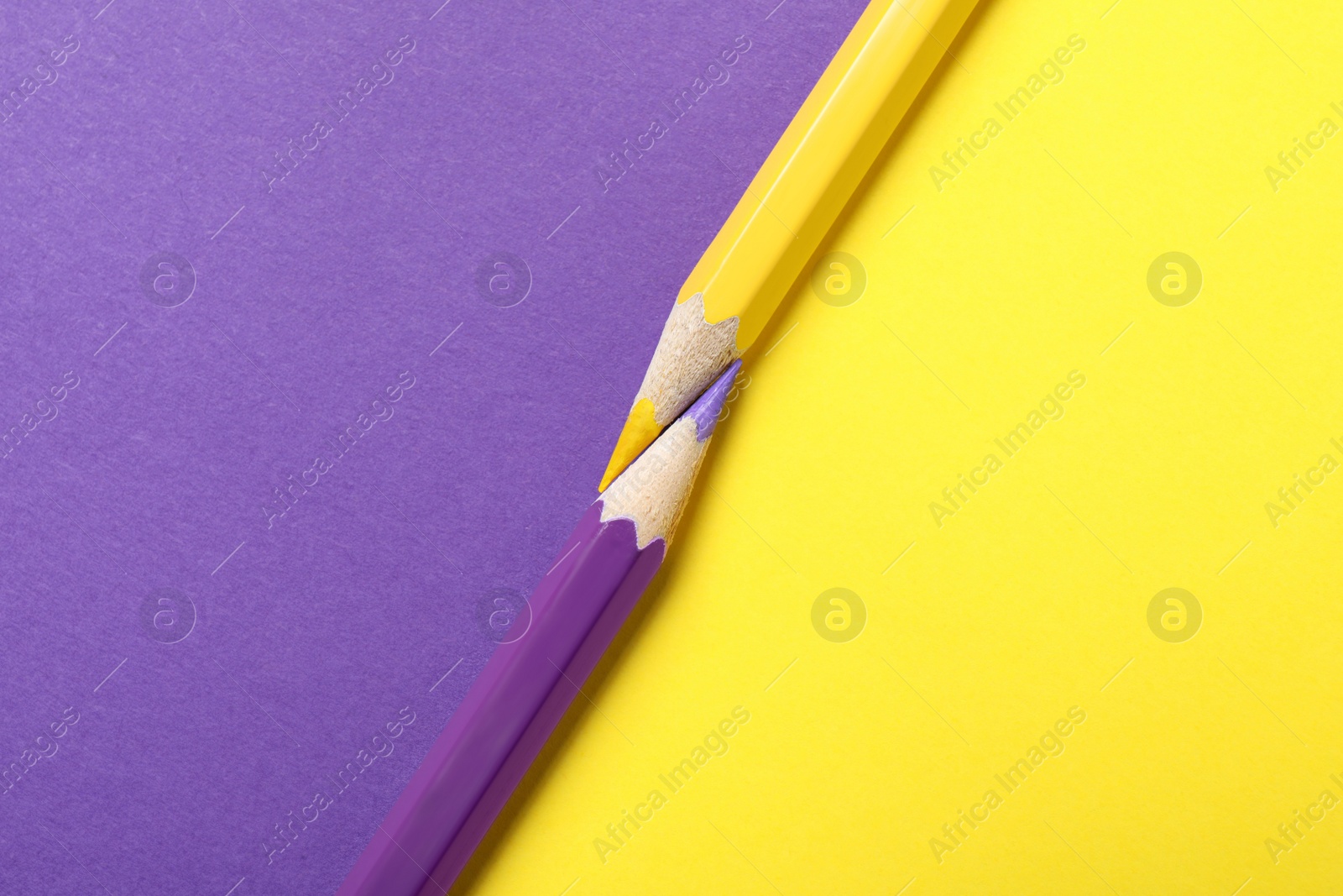 Photo of Two pencils on yellow and purple background, top view