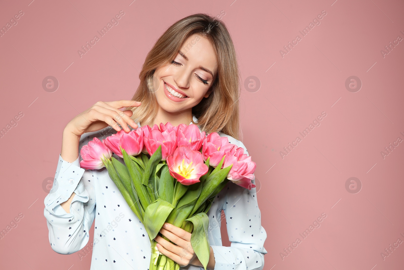 Photo of Portrait of beautiful smiling girl with spring tulips on pink background. International Women's Day