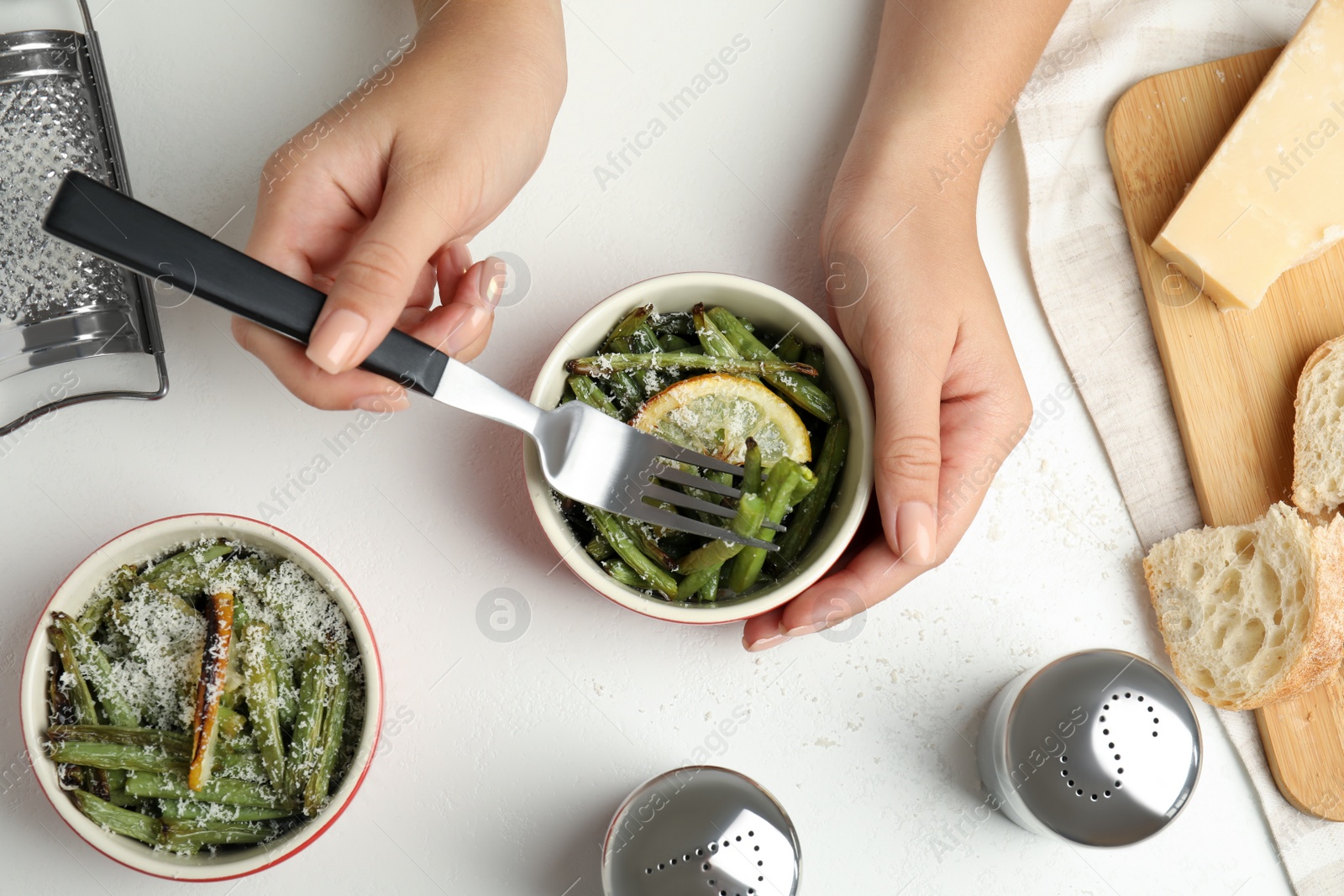 Photo of Woman eating delicious baked green beans at white table, top view