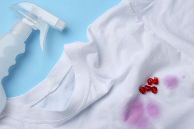 Photo of White shirt with fruit juicy stains, detergent and pomegranate seeds on light blue background, flat lay