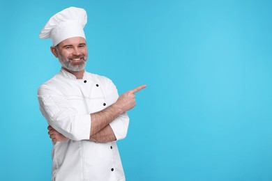 Photo of Happy chef in uniform pointing at something on light blue background, space for text