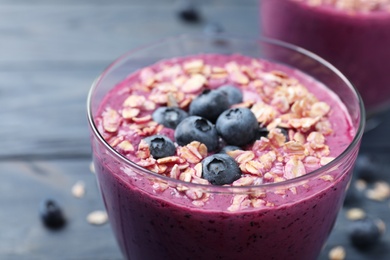 Glass with delicious blueberry smoothie with granola on blue wooden table, closeup