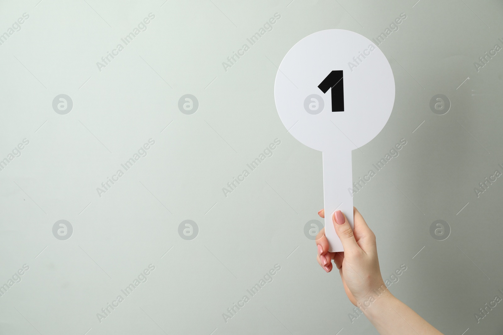 Photo of Woman holding auction paddle with number 1 on light grey background, closeup. Space for text