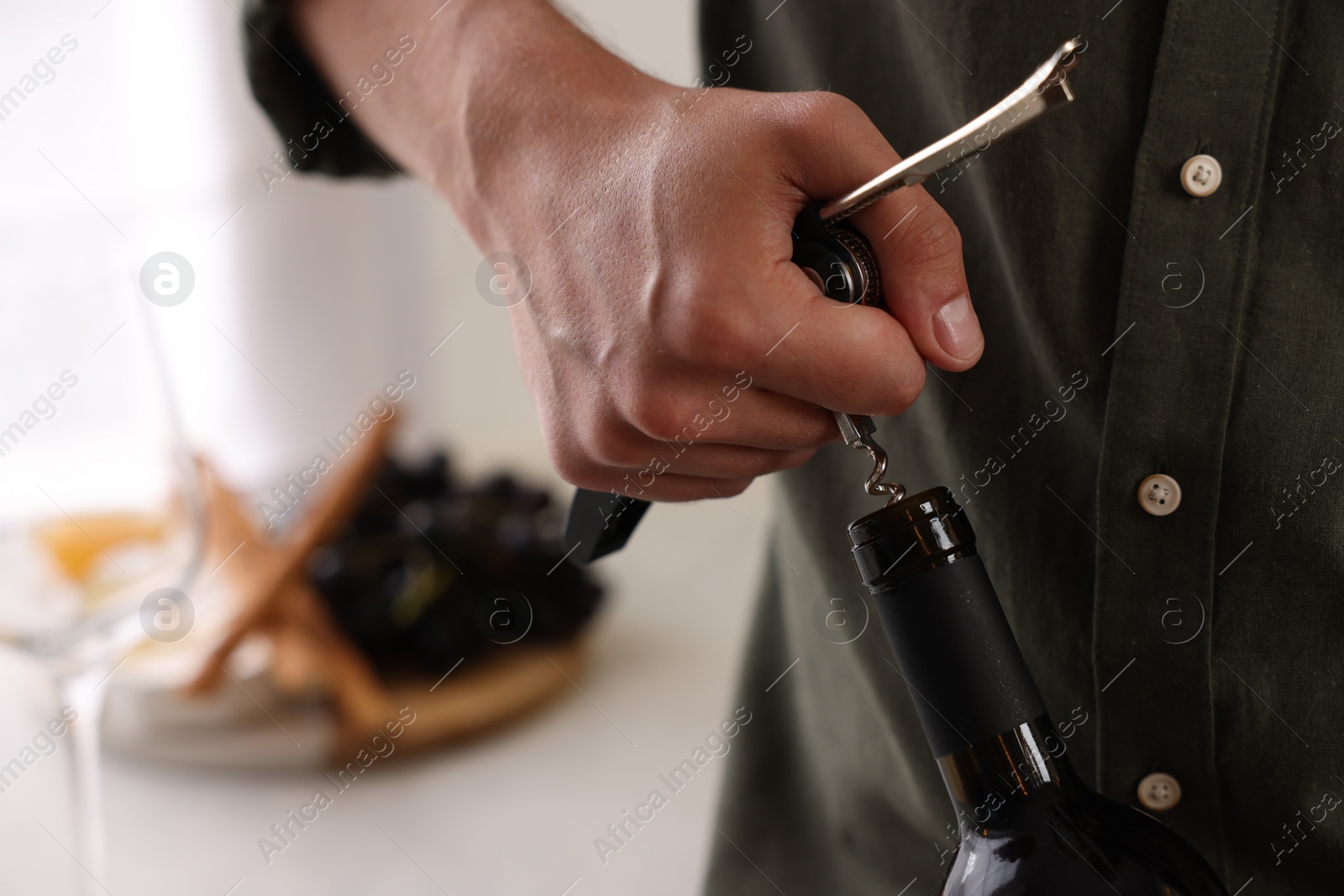 Photo of Man opening wine bottle with corkscrew indoors, closeup. Space for text