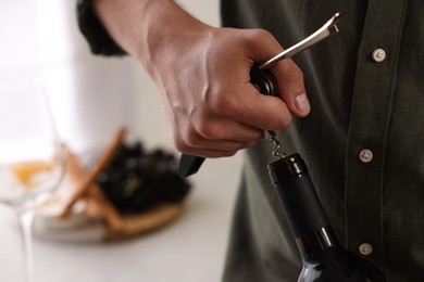 Photo of Man opening wine bottle with corkscrew indoors, closeup. Space for text