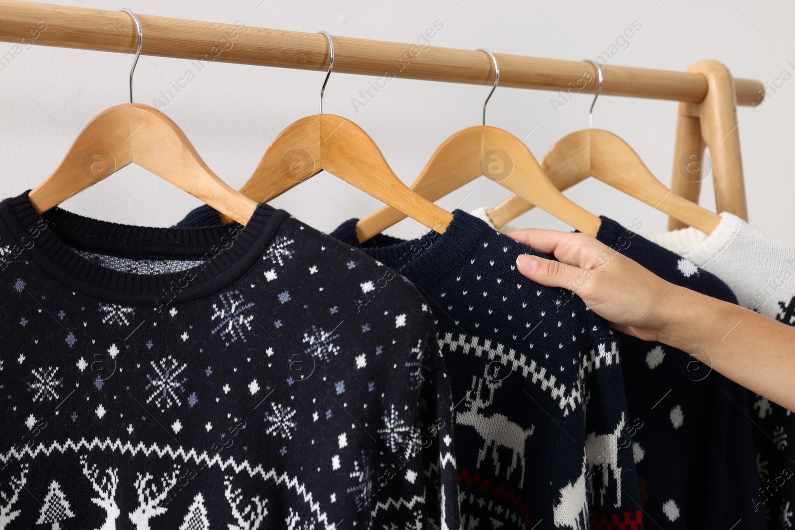 Photo of Woman choosing Christmas sweater from rack near white wall, closeup