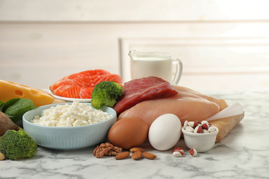 Photo of Different products rich in protein on white marble table