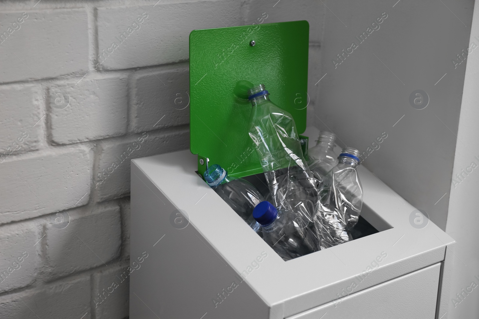 Photo of Many used plastic bottles in metal bin near white brick wall. Recycling problem