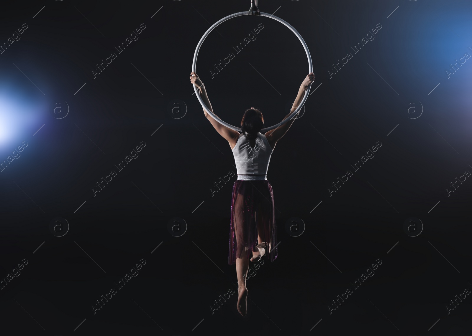 Photo of Young woman performing acrobatic element on aerial ring indoors