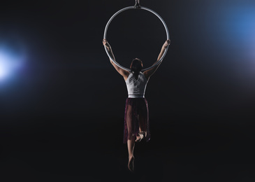 Photo of Young woman performing acrobatic element on aerial ring indoors