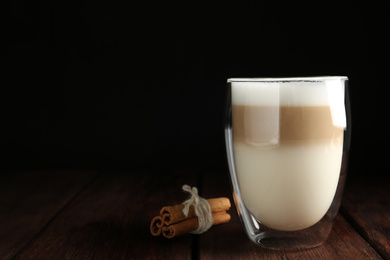 Photo of Delicious latte macchiato and cinnamon on wooden table against black background. Space for text