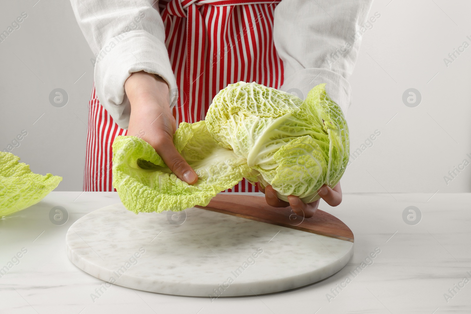 Photo of Woman separating leaf from fresh savoy cabbage at white marble table, closeup