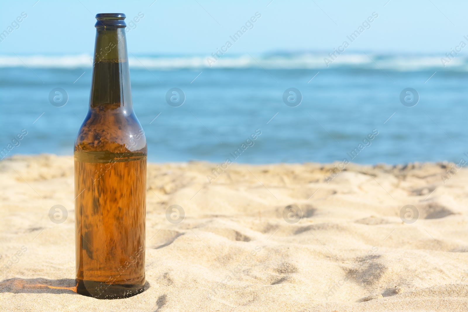 Photo of Bottle of beer on sandy beach near sea. Space for text