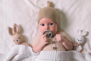 Cute newborn baby with pacifier and toys on white knitted plaid, top view