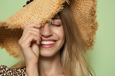 Photo of Beautiful young woman wearing straw hat on light green background, closeup. Stylish headdress