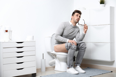 Photo of Thoughtful man sitting on toilet bowl in bathroom