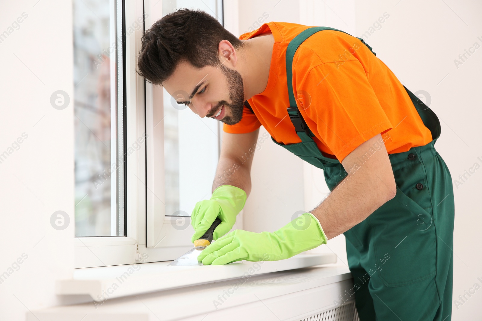 Photo of Professional young janitor cleaning windowsill in room