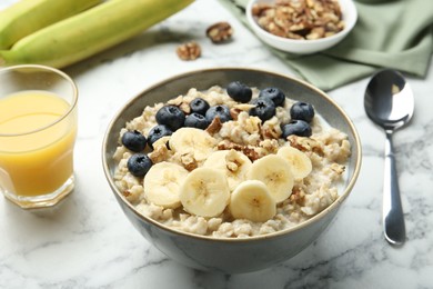Tasty oatmeal with banana, blueberries, walnuts and milk served in bowl on white marble table