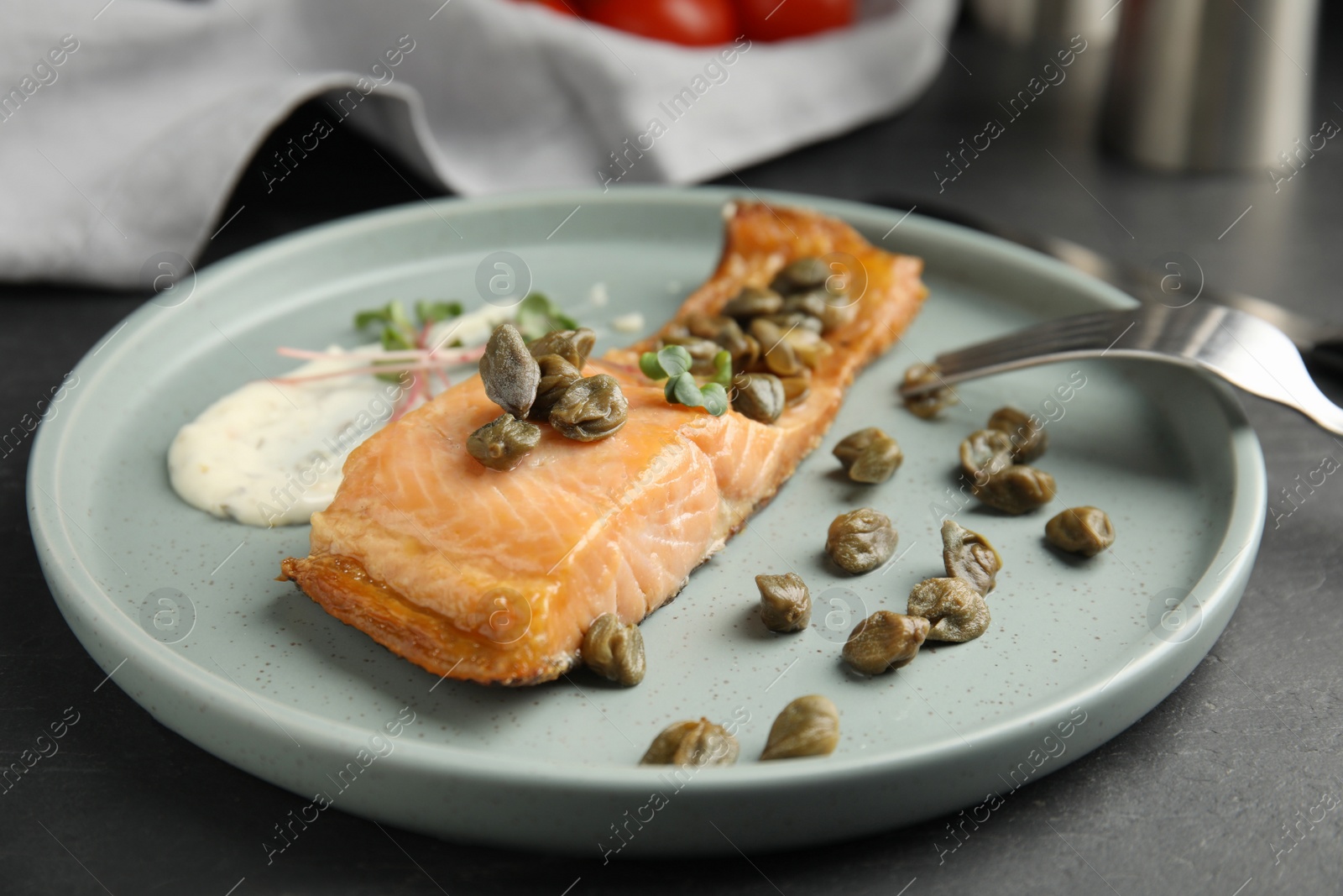 Photo of Delicious salmon with capers and sauce served on dark table, closeup