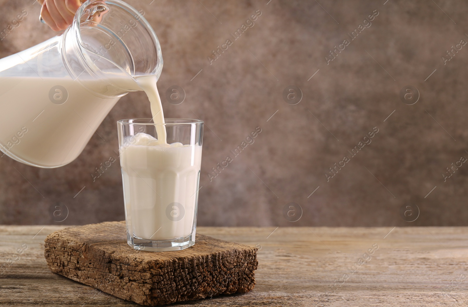 Photo of Woman pouring fresh milk into glass at wooden table, closeup. Space for text