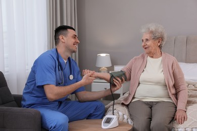 Photo of Young caregiver measuring blood pressure of senior woman in bedroom. Home health care service
