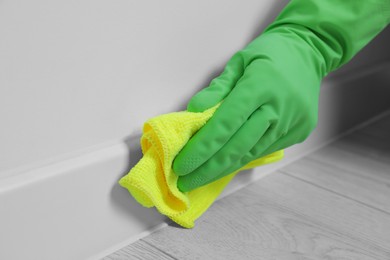Photo of Woman in gloves cleaning plinth with cloth indoors, closeup