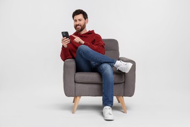 Photo of Happy man with smartphone sitting on armchair against white background