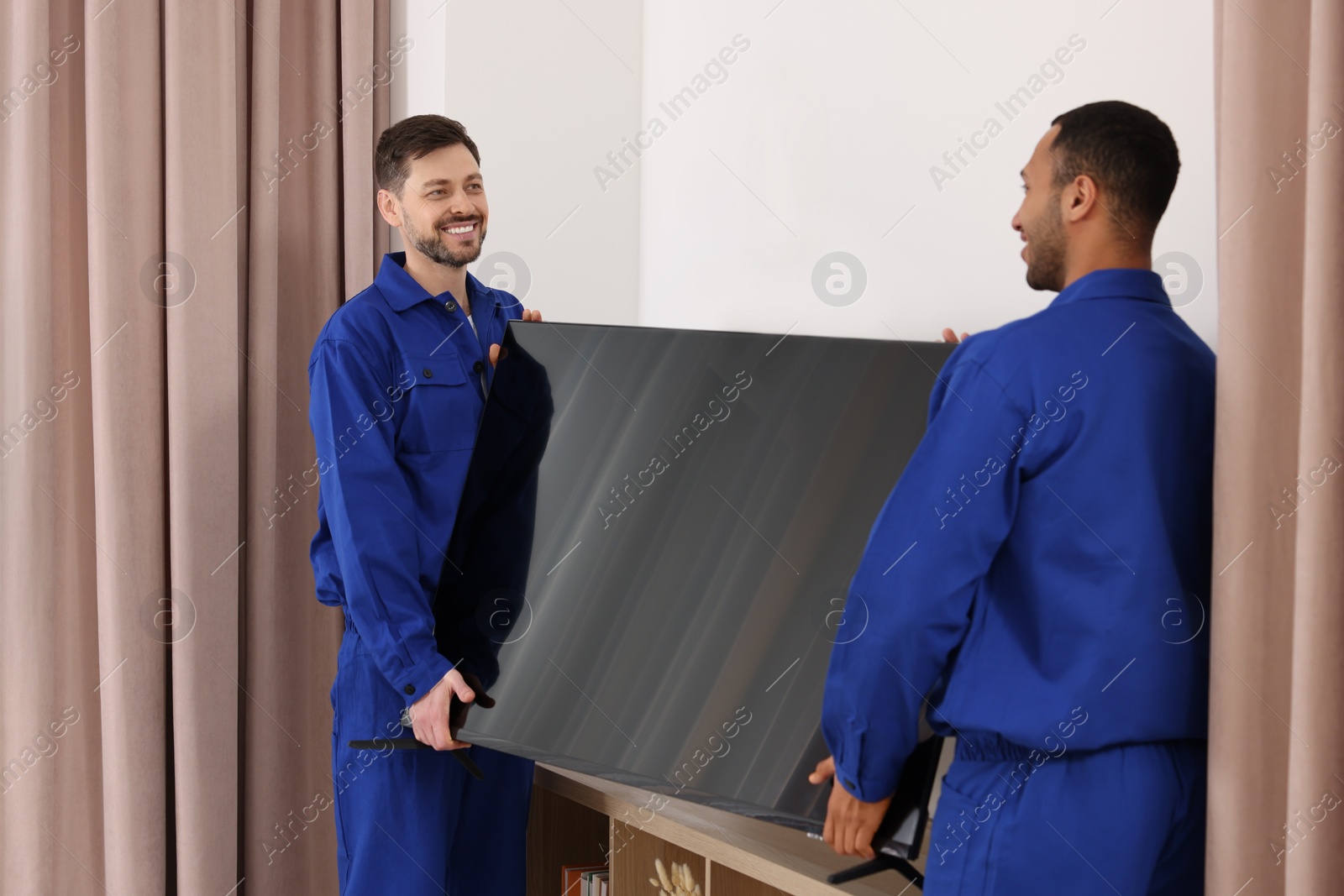 Photo of Male movers installing plasma TV near white wall in new house