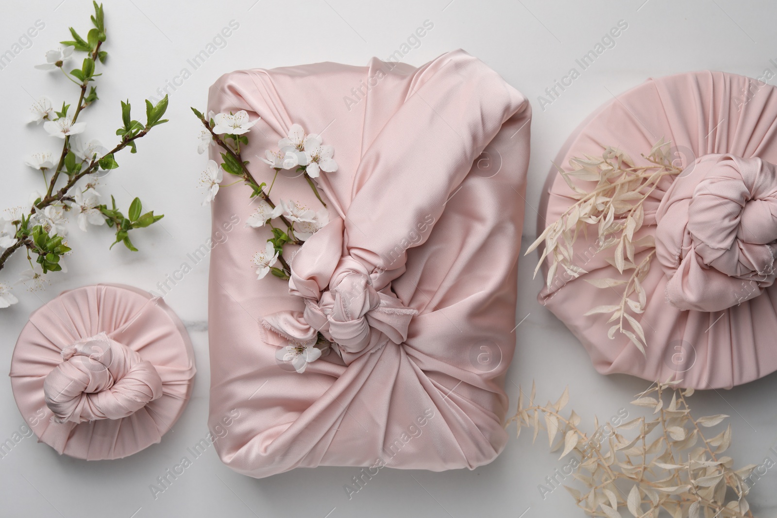 Photo of Furoshiki technique. Gifts packed in pink fabric with beautiful knots on white marble table, flat lay