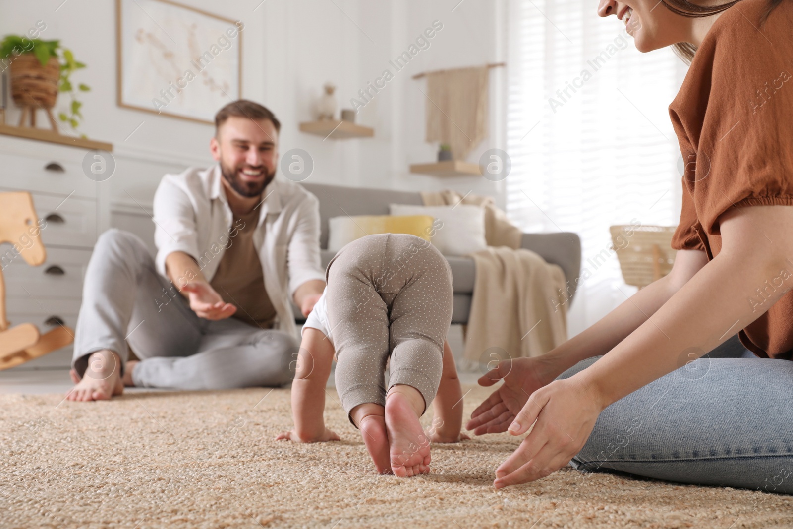 Photo of Happy parents watching their baby crawl on floor at home