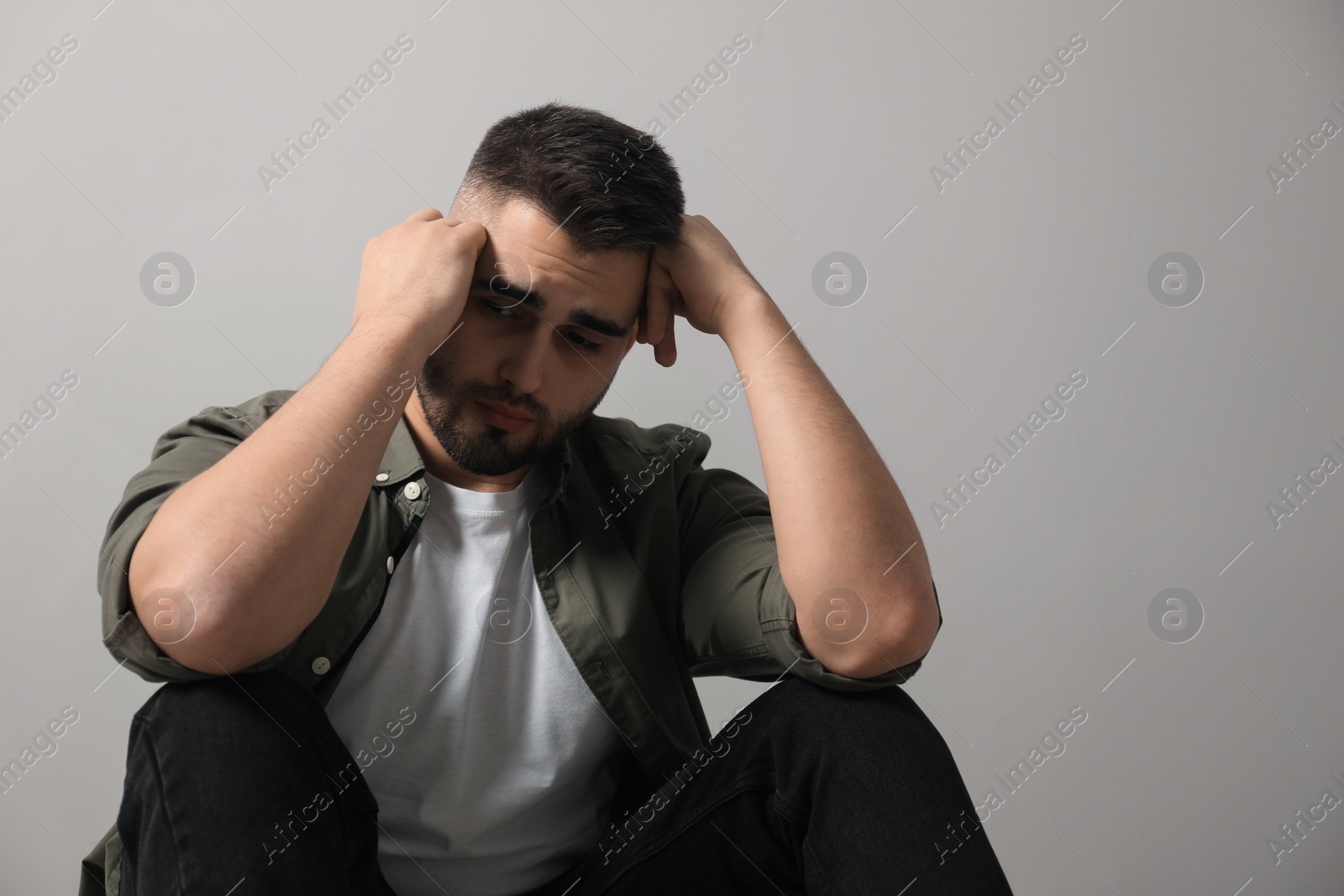 Photo of Sad man sitting near light grey wall. Space for text