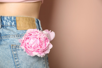 Woman with pink peony in pocket on beige background, closeup. Space for text