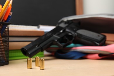 Gun, bullets and school stationery on wooden table, closeup. Space for text