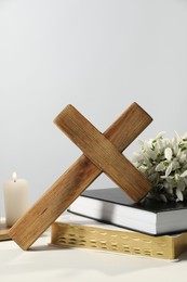 Photo of Wooden cross, ecclesiastical books, church candle and flowers on white table