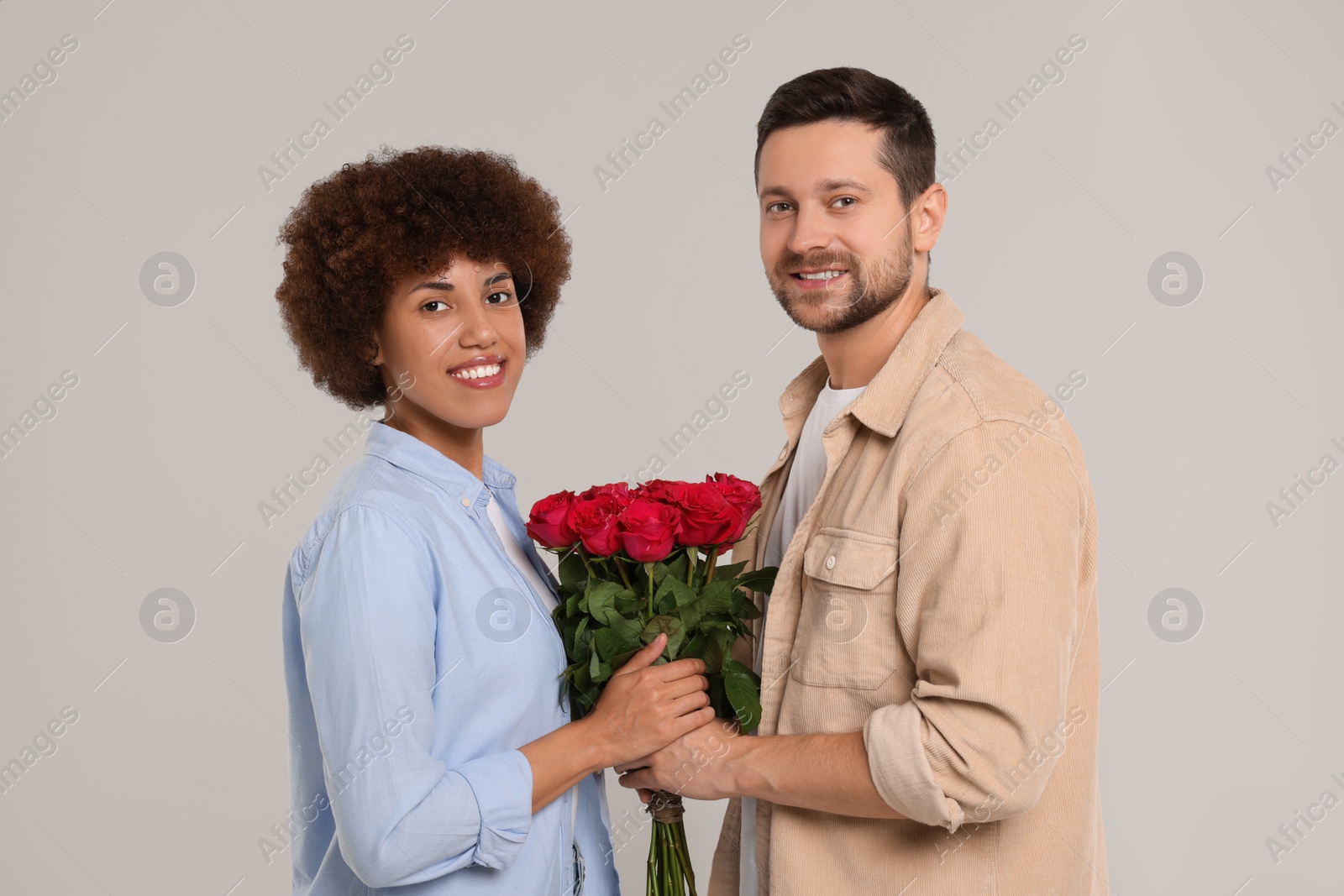 Photo of International dating. Happy couple with bouquet of roses on light grey background