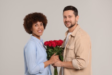 Photo of International dating. Happy couple with bouquetroses on light grey background