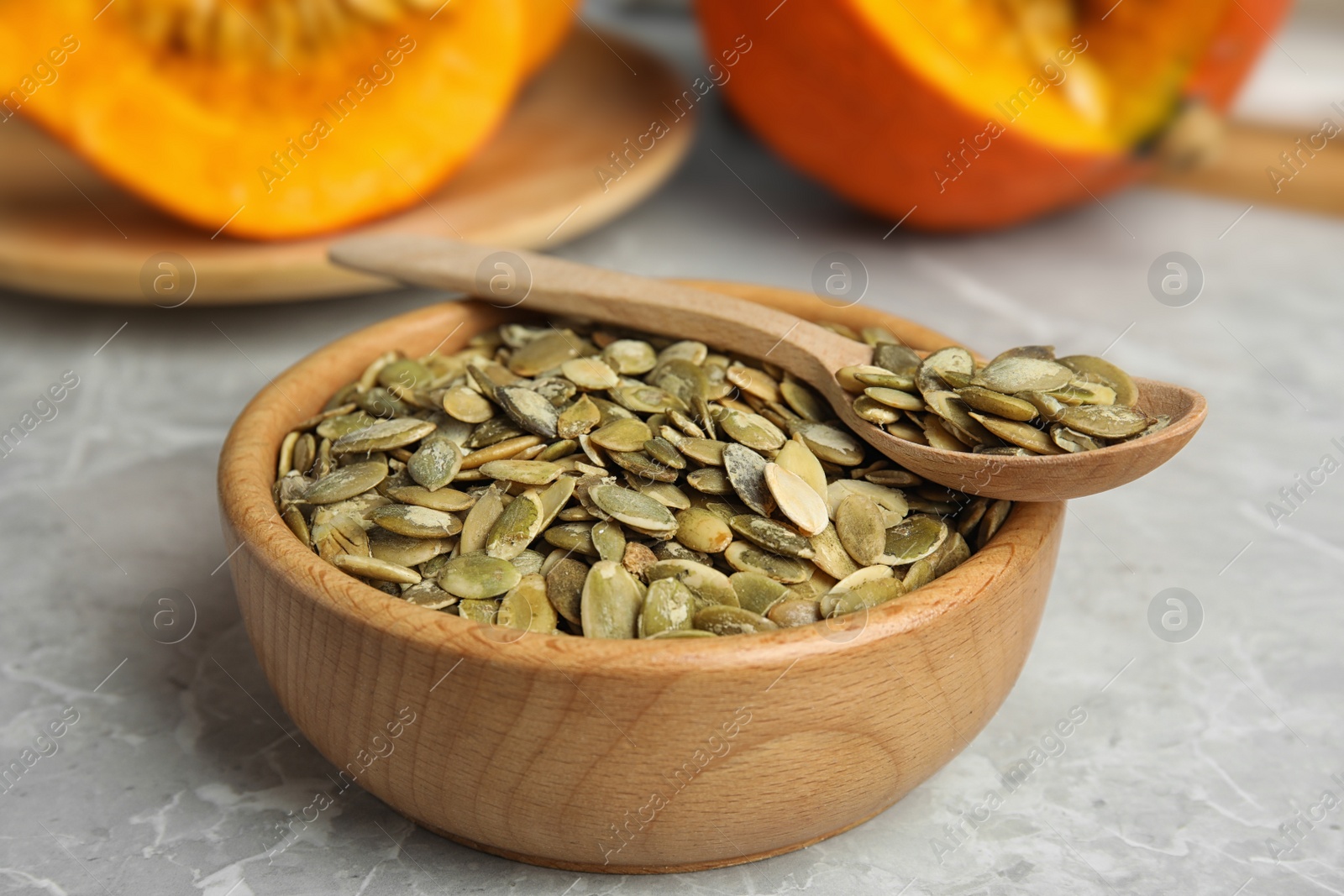 Photo of Bowl and spoon of raw pumpkin seeds on light grey marble table