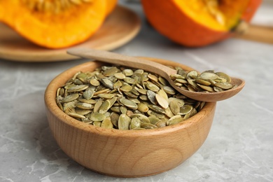 Photo of Bowl and spoon of raw pumpkin seeds on light grey marble table