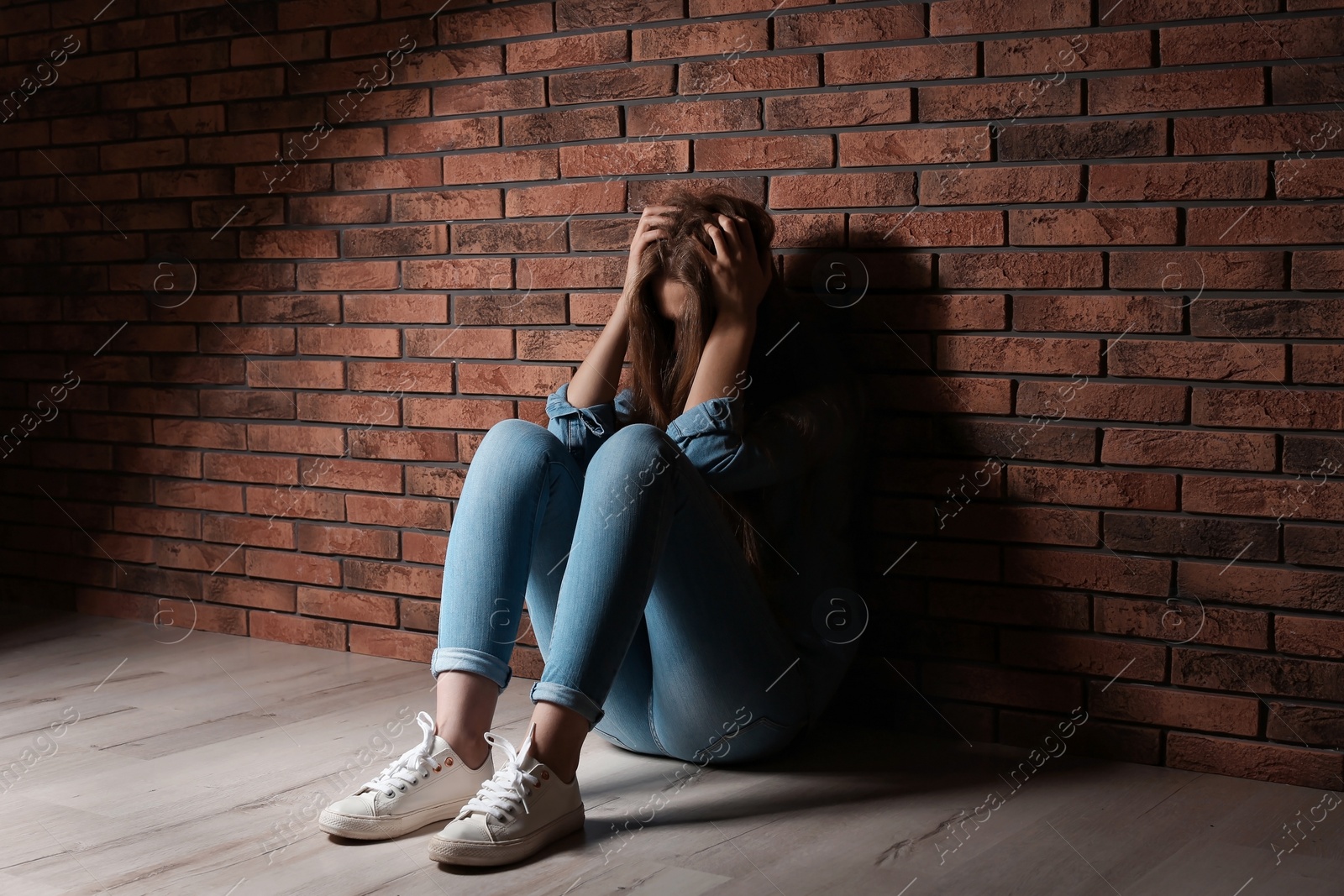 Photo of Depressed young woman sitting on floor near brick wall