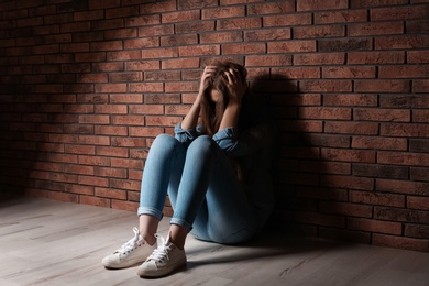Depressed young woman sitting on floor near brick wall
