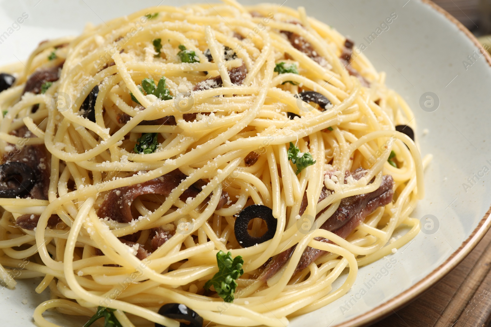 Photo of Delicious pasta with anchovies, olives and parmesan cheese on wooden table, closeup