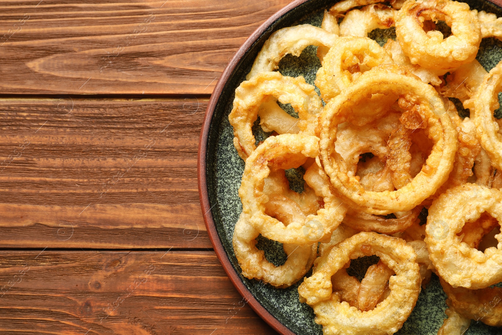 Photo of Homemade crunchy fried onion rings on wooden table, top view. Space for text