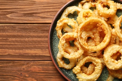 Homemade crunchy fried onion rings on wooden table, top view. Space for text