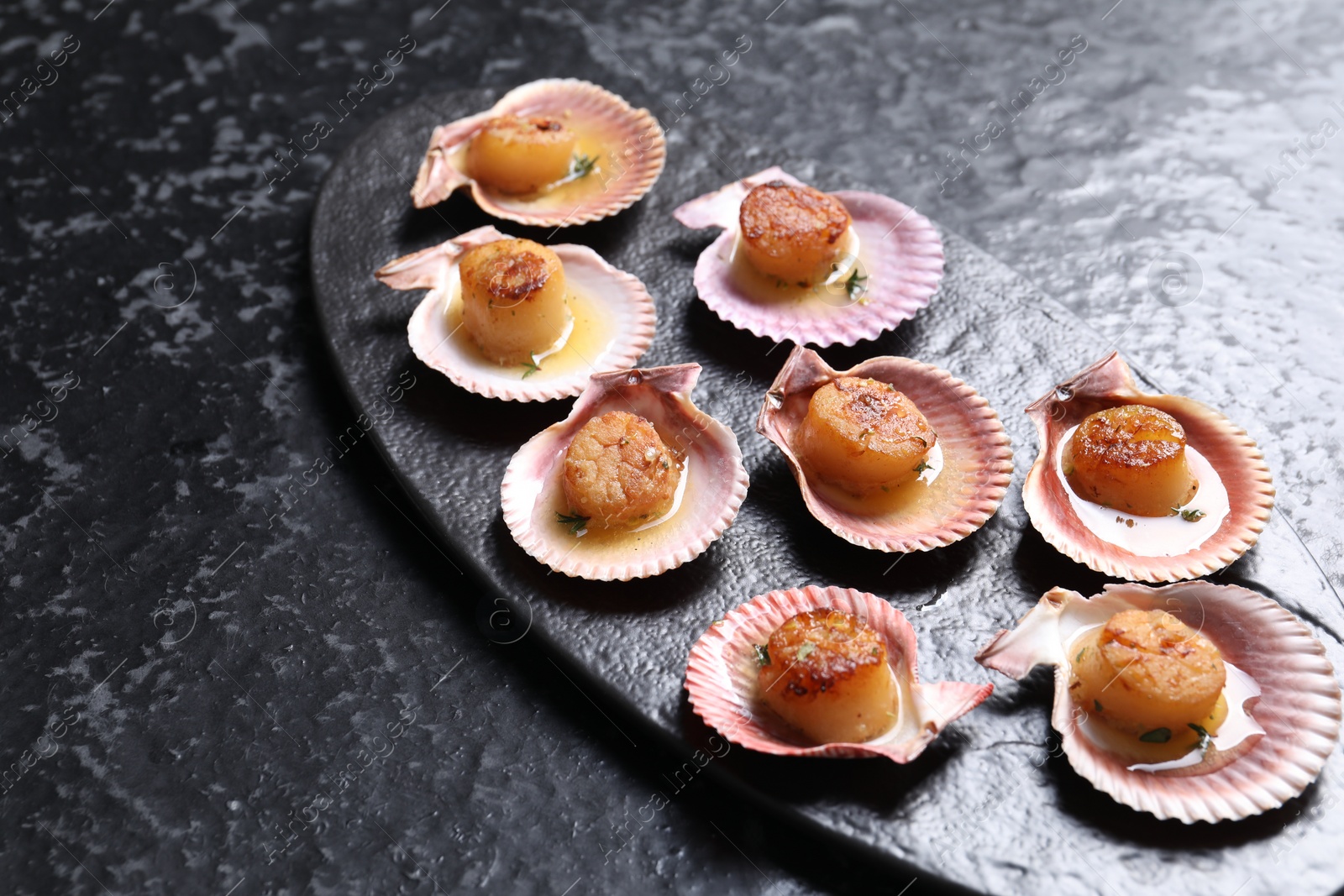 Photo of Delicious fried scallops in shells on black table, closeup