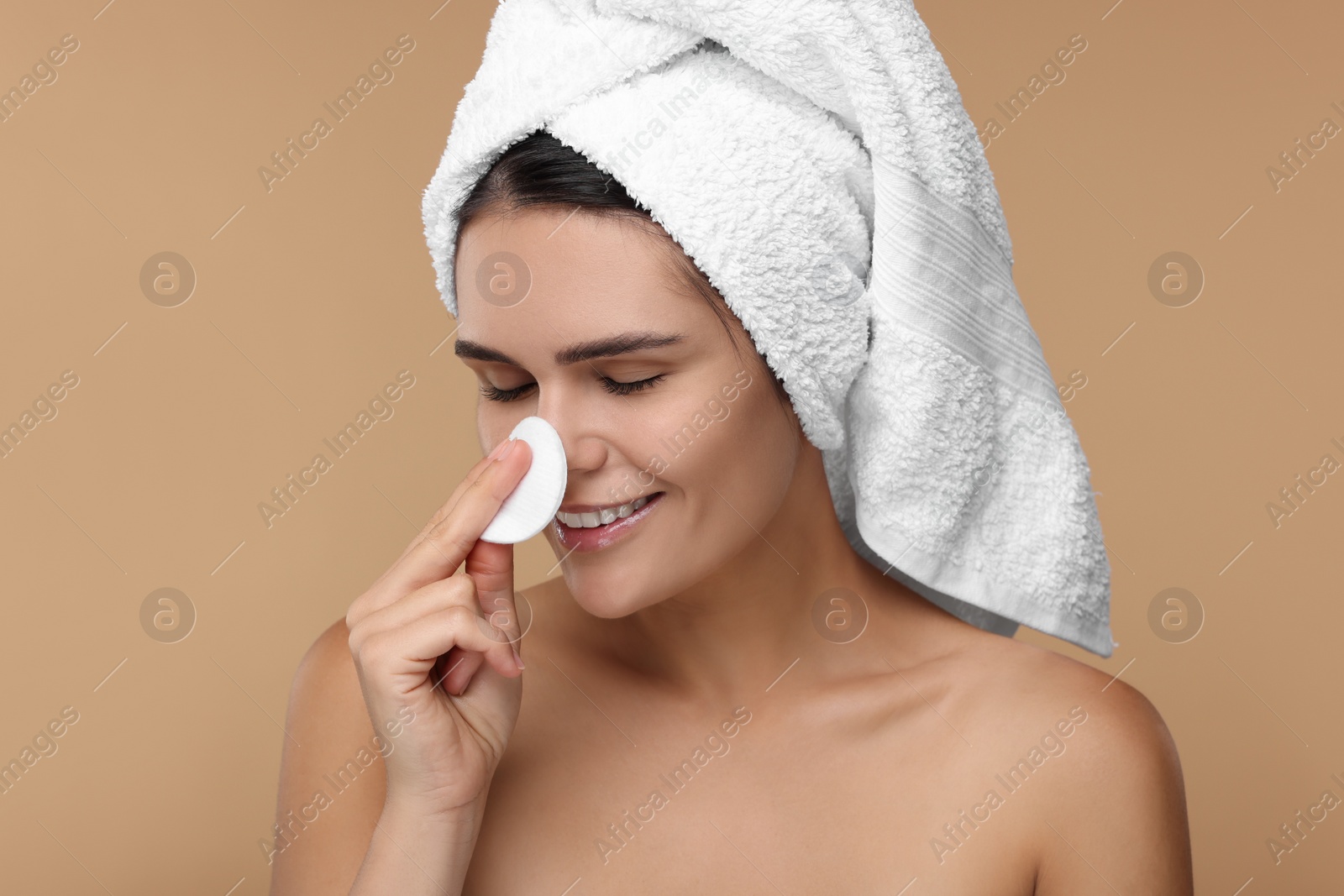 Photo of Young woman cleaning her face with cotton pad on beige background