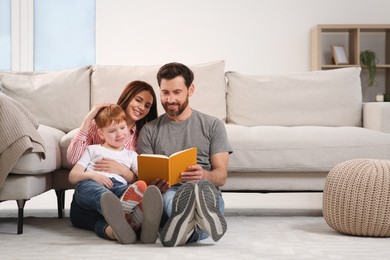Photo of Happy parents with their child reading book on floor at home, space for text