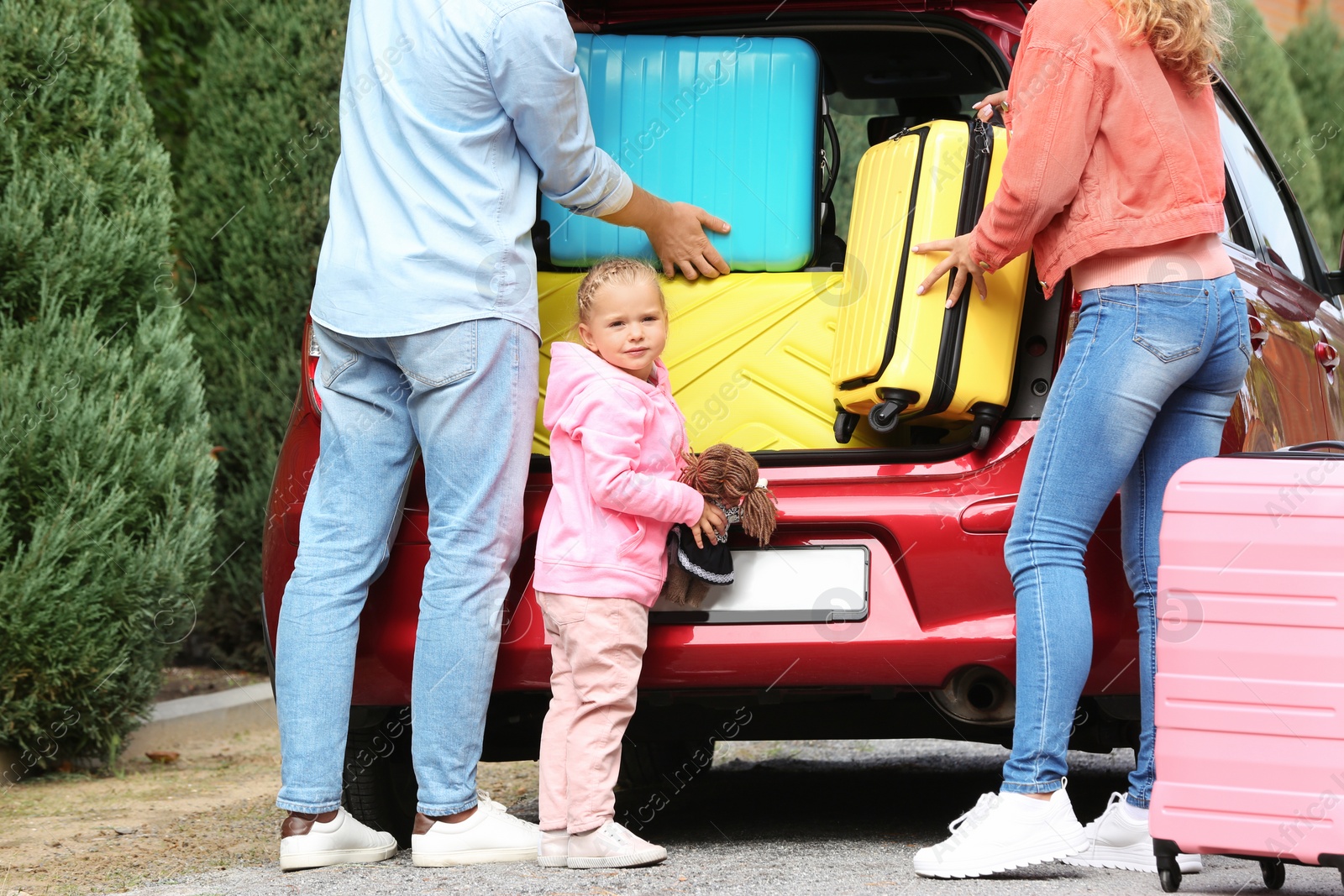 Photo of Young family loading suitcases in car trunk outdoors