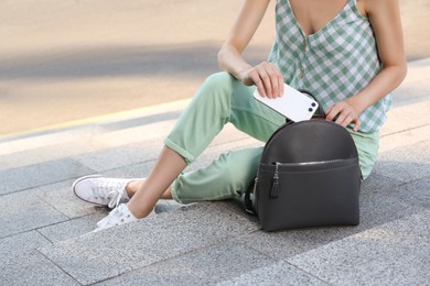 Photo of Young woman with stylish backpack and smartphone on stairs outdoors, closeup