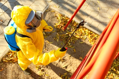 Photo of Person in hazmat suit with disinfectant sprayer cleaning children's playground, above view. Surface treatment during coronavirus pandemic