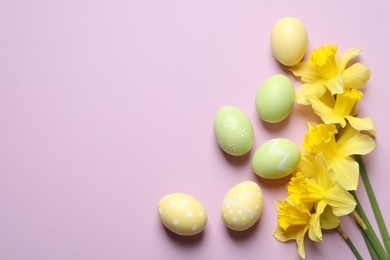 Flat lay composition of painted Easter eggs and flowers on color background, space for text